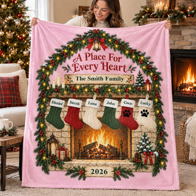 Personalized blanket custom family name in pink held up by a smiling woman, six stockings by a lit fireplace