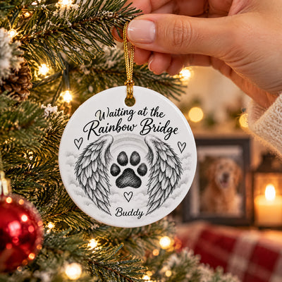 Personalized pet memorial ceramic ornament held by hand over a Christmas tree, framed dog photo behind